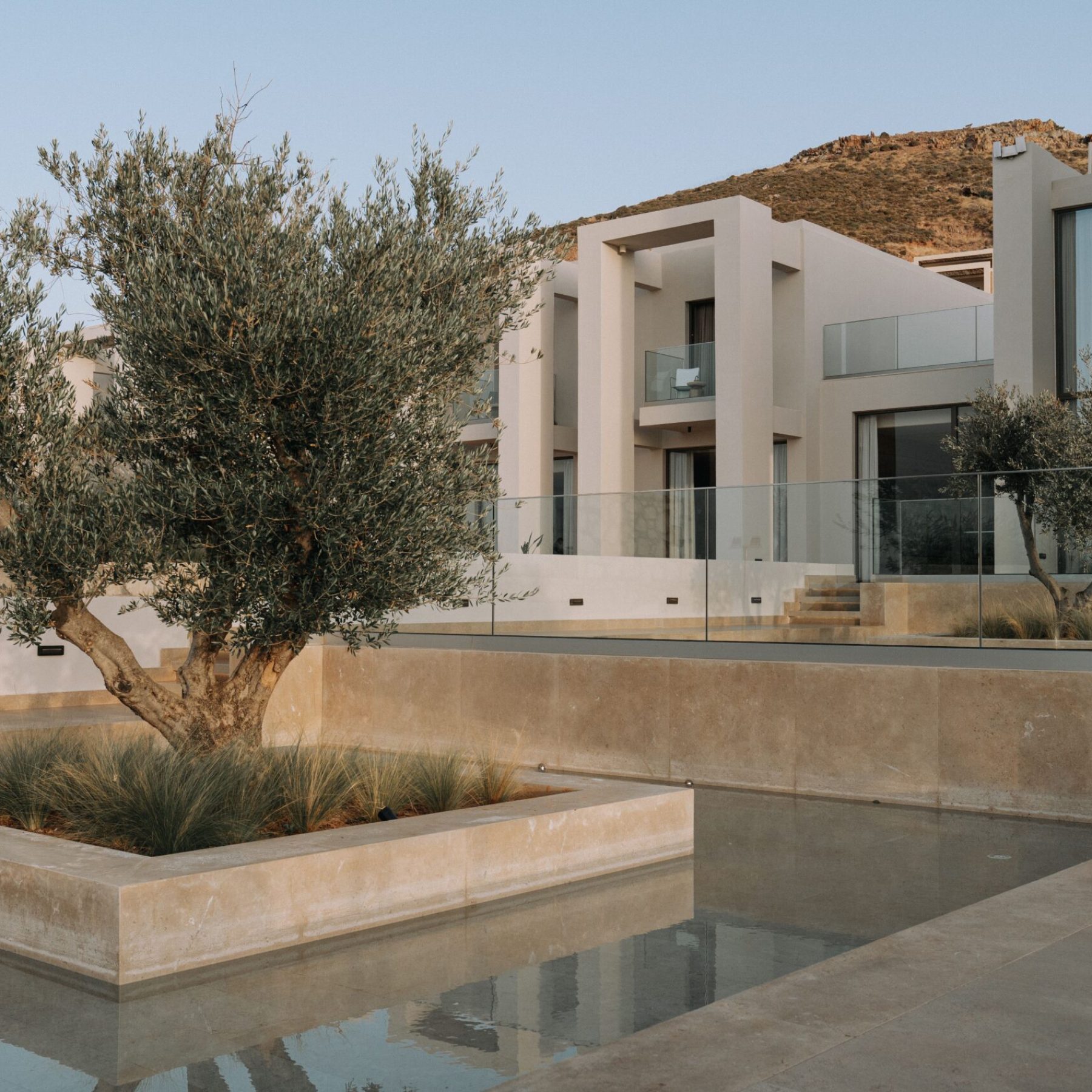 Modern luxury house exterior with glass facade, landscaped garden, and water feature.